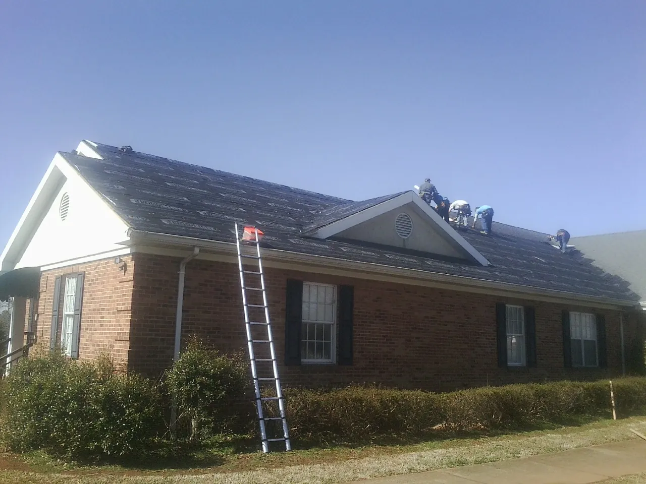 Crew tearing shingles off a brick ranch roof with a ladder set — Metal Roof Repair work by our crew in Stem