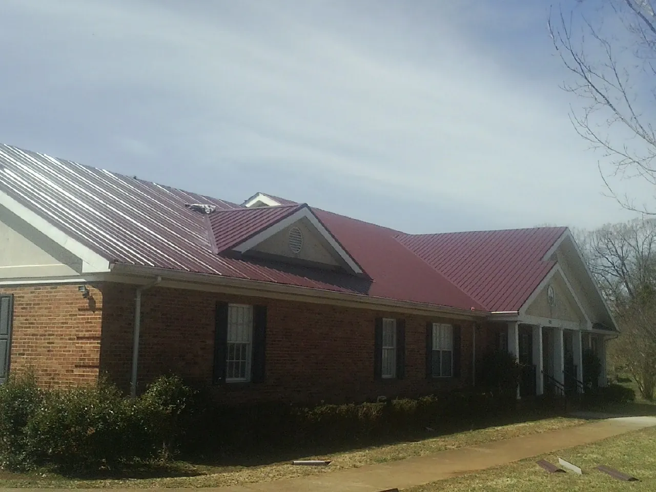 Red metal roof with gabled entries on a long brick building, from a Hail Damage Roof Repair job in Stem