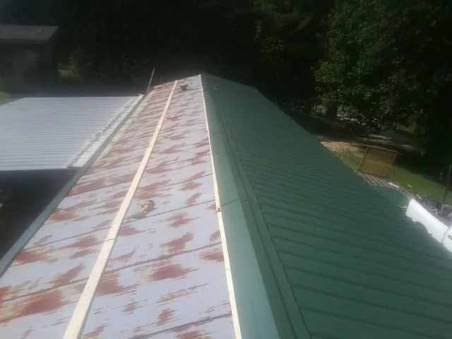 Old rusted panels beside newly installed green metal roofing — Wind Damage Roof Repair by Roofing Brothers in Stem
