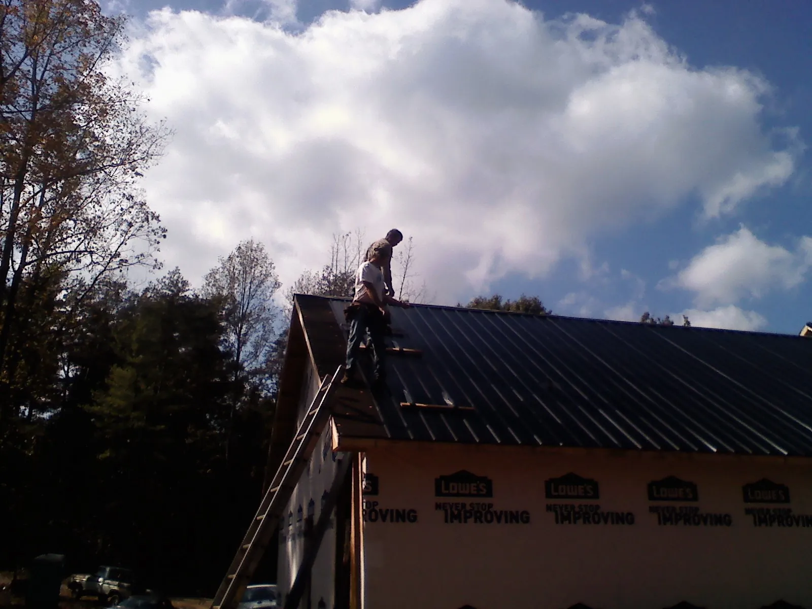 Roofer fastening dark metal panels high against a cloudy sky, from a Roof Inspection job in Stem