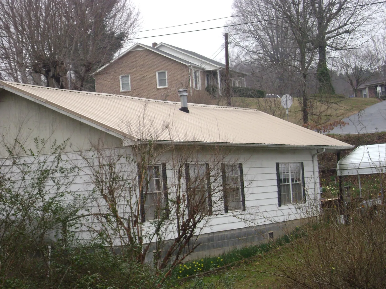 Tan metal roof on a white sided house set into a hillside — Commercial Roofing by Roofing Brothers in Stem
