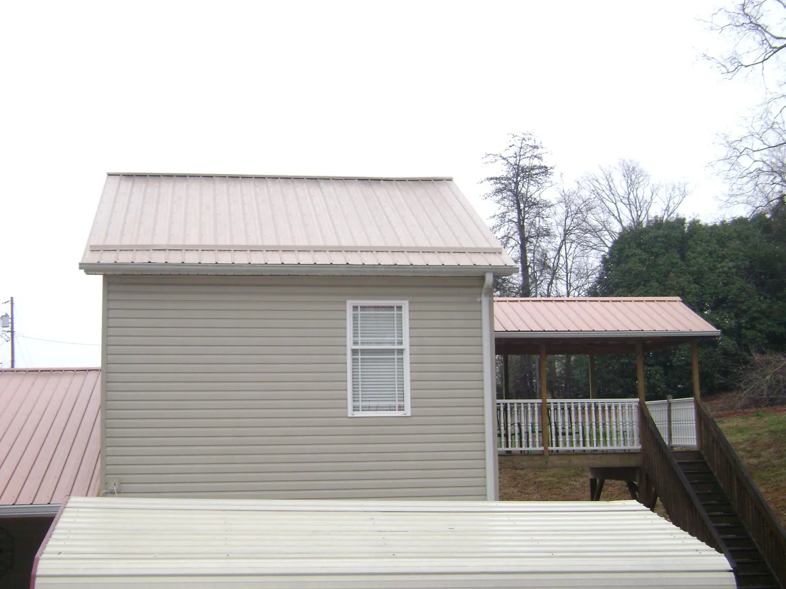 Tan metal roofs on a two story addition and attached porch, from a Roof Replacement job in Stem